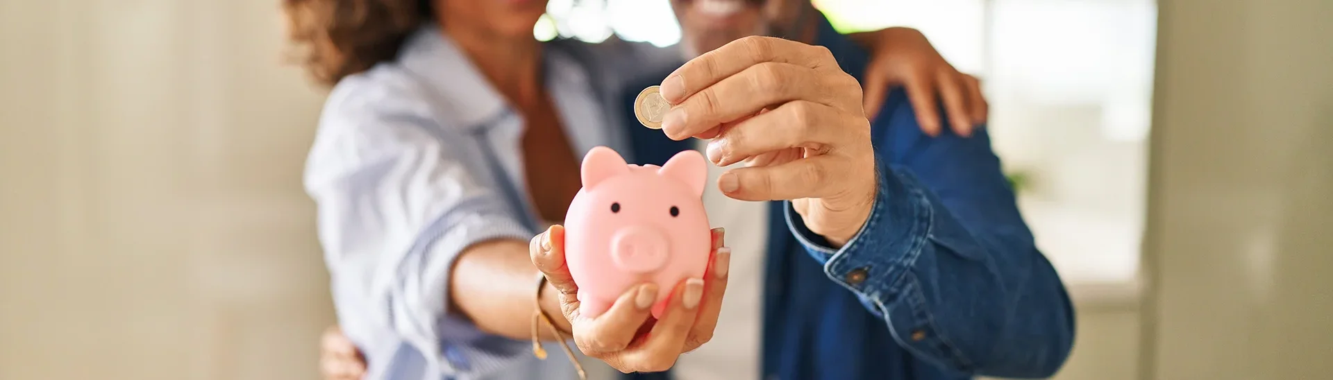 Two people holding a piggie bank with one putting a quarter into the top of the bank.