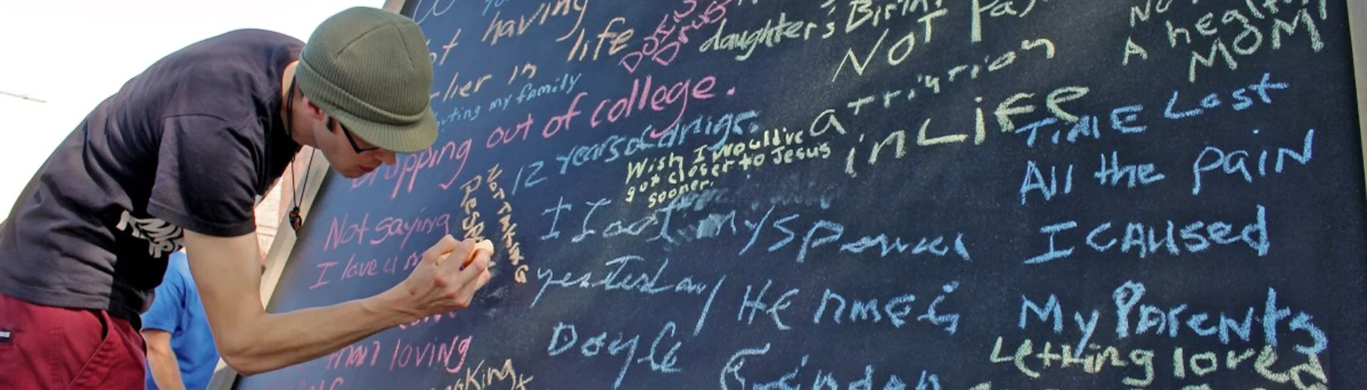 A man with glasses and a hat is writing on a chalkboard.