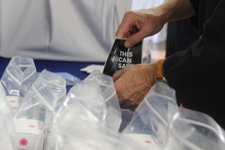 A man stuffing a NARCAN flyer into a plastic bag.