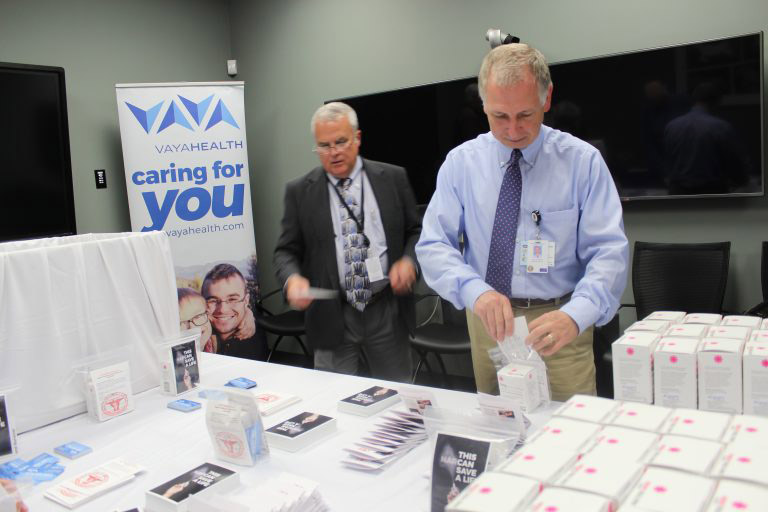 Two men with ties on working to stuff bags with NARCAN and flyers.