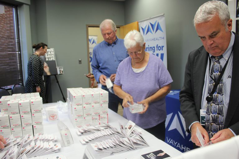 Several older men and a woman working to fill plastic bags with NARCAN.