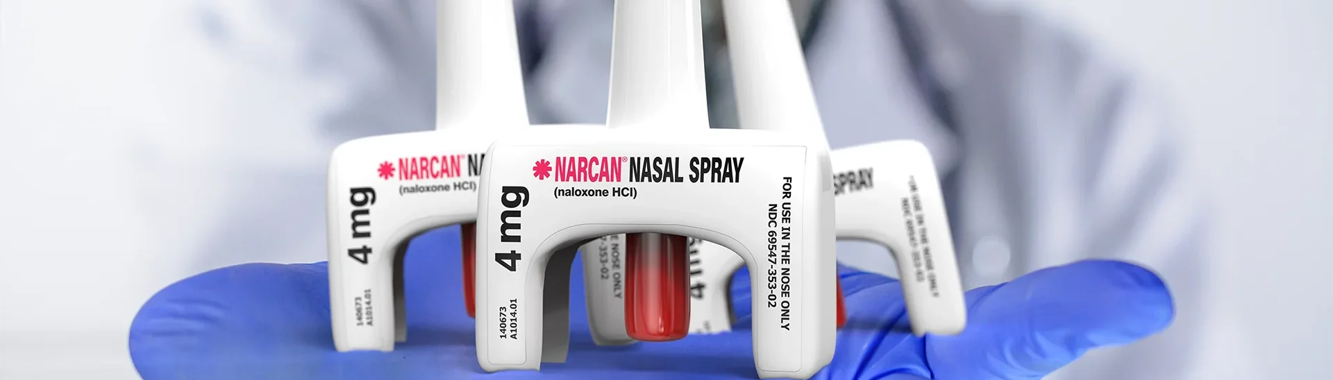 A doctor wearing blue gloves is holding three NARCAN inhalers.