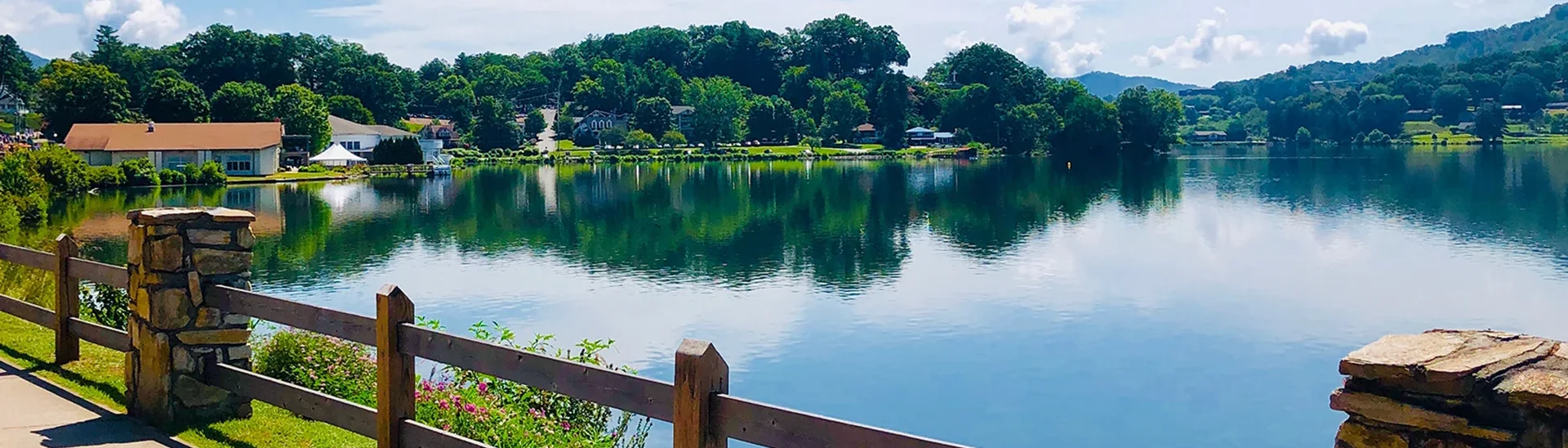 Scenic view of Lake Junaluska in North Carolina includes a walking path with wood fence posts and building off in the distance.