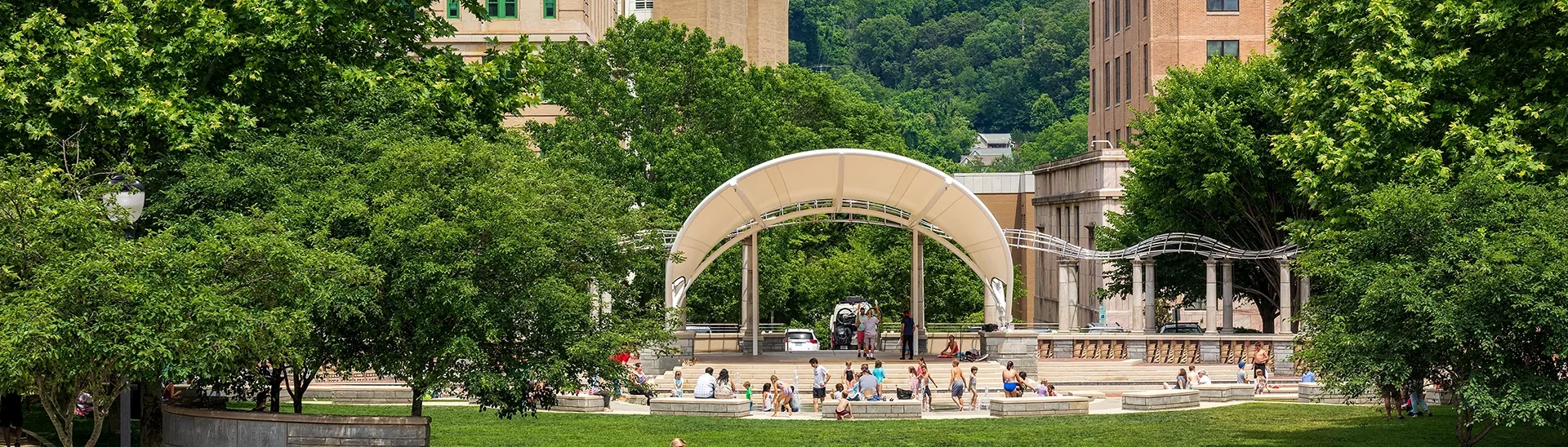 Children playing in downtown Asheville, NC park while adults ride bikes or walk through the scene.