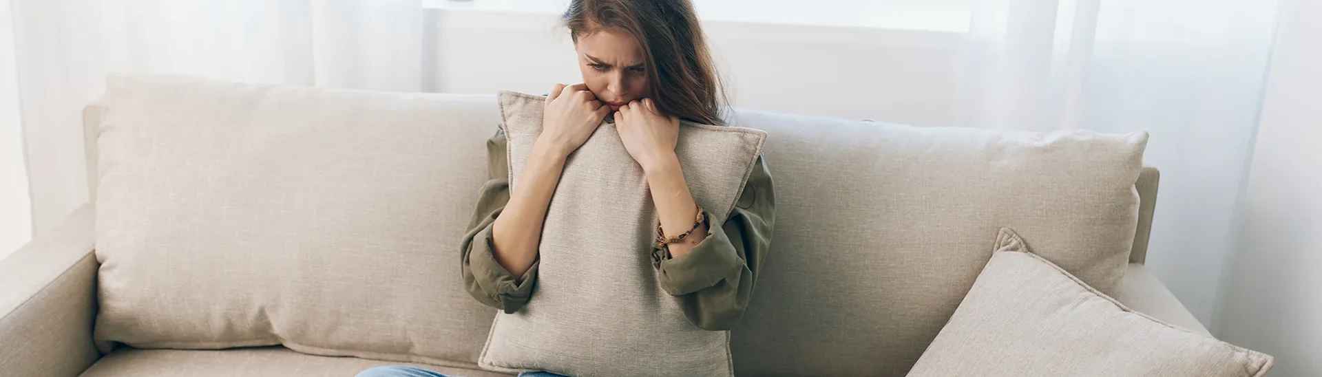 A woman stressed and need of help sits on a couch clutching a pillow within her arms.