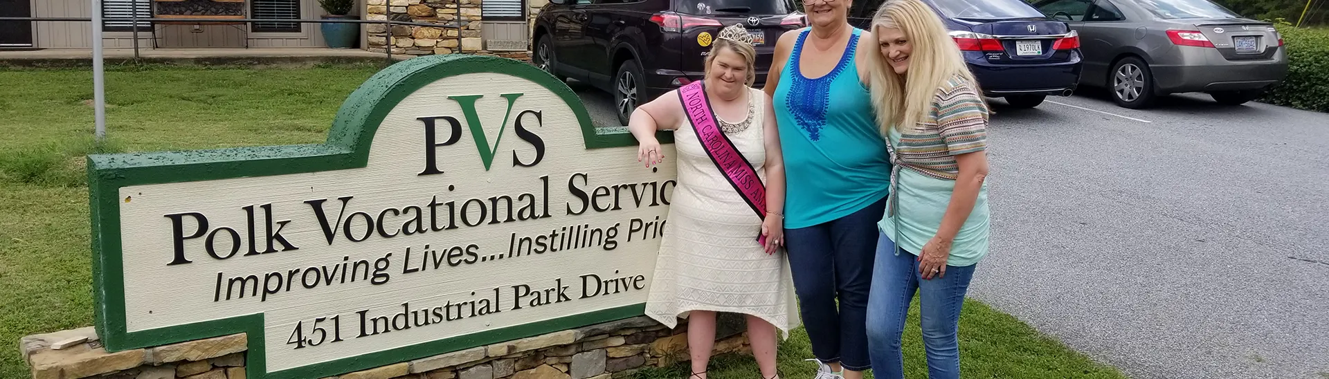 Tres mujeres sonríen junto a un cartel en el que se lee PVS Vocational Service.