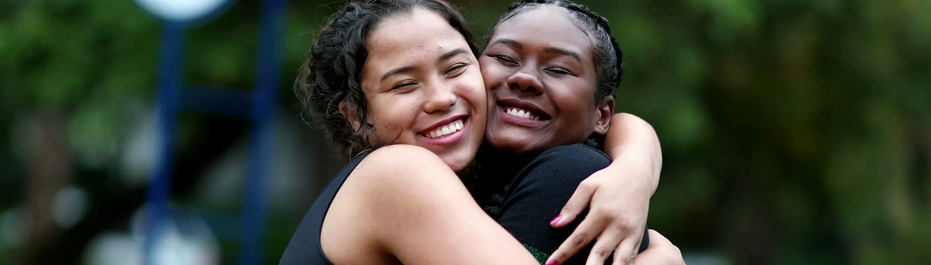 Two woman hugging and smiling with their arms wrapped around each other.