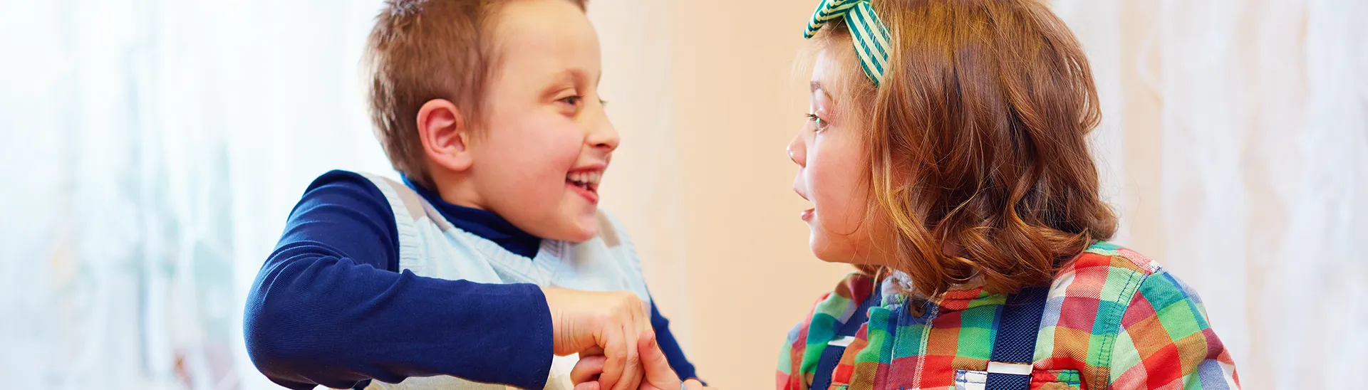 Dos niños, un niño sonriente a la izquierda y una niña con un lazo verde en el pelo a la izquierda, hablan juntos.