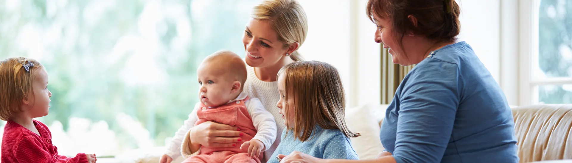 Two women, one with a baby in her lap and two other children smiling and talking together.