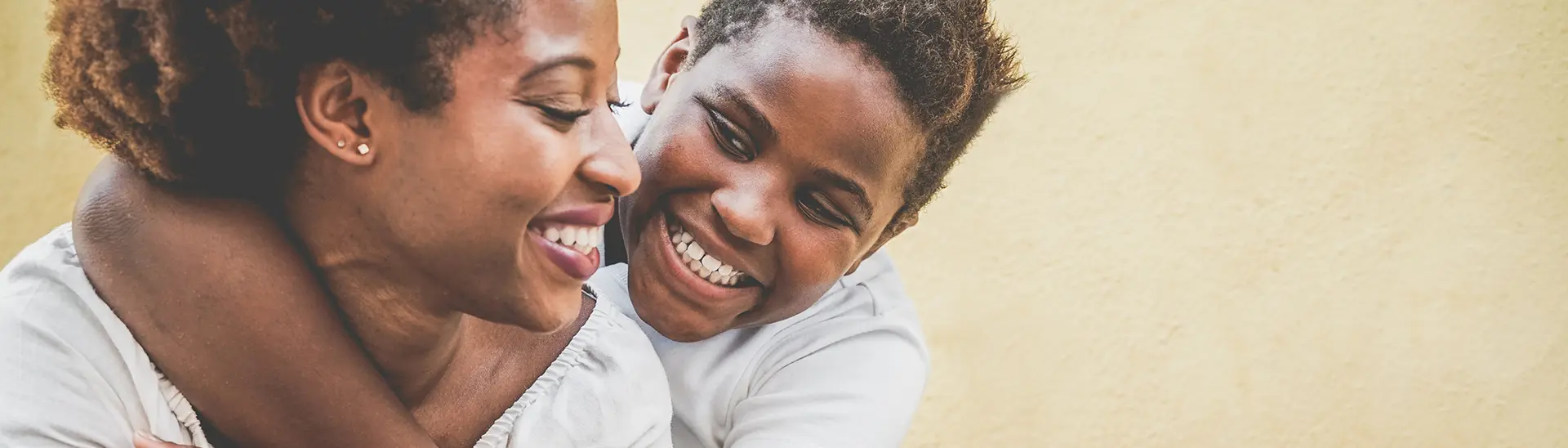 Son and mother smiling at each other. The son's arm is wrapped around mother's neck.