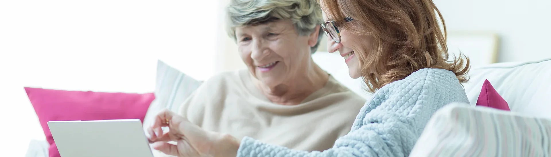 A caregiver working with an elderly woman using a laptop to show information.