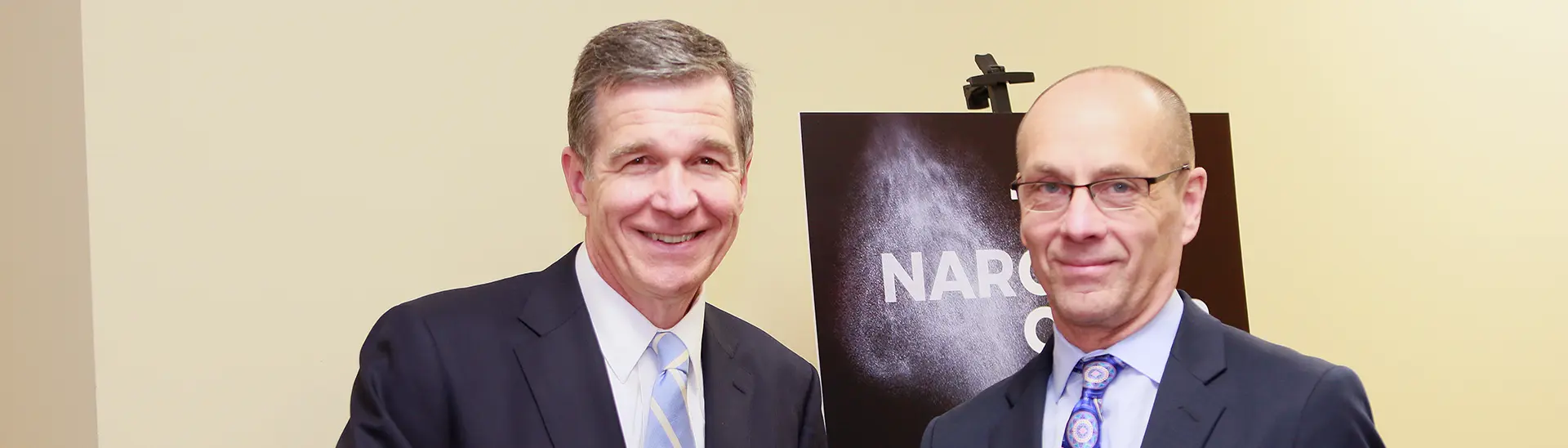 El gobernador de Carolina del Norte, Roy Cooper, estrecha la mano del director general de Vaya Health, Brian Ingraham.