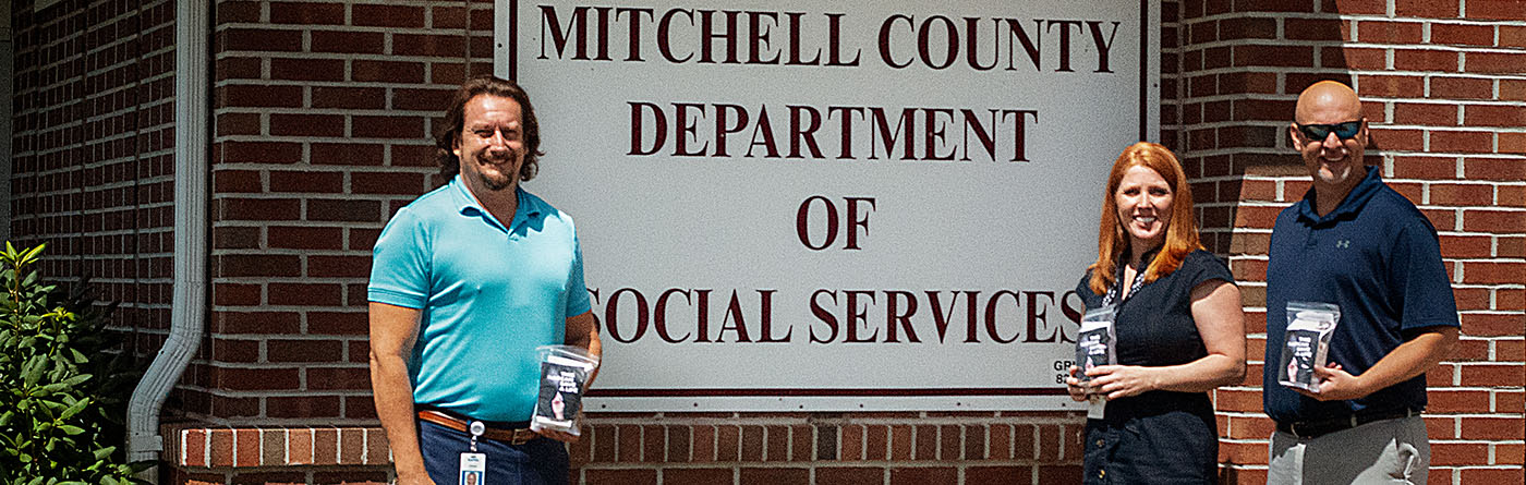 Two men and a woman stand in from of the sign for the Department of Social Services smiling.