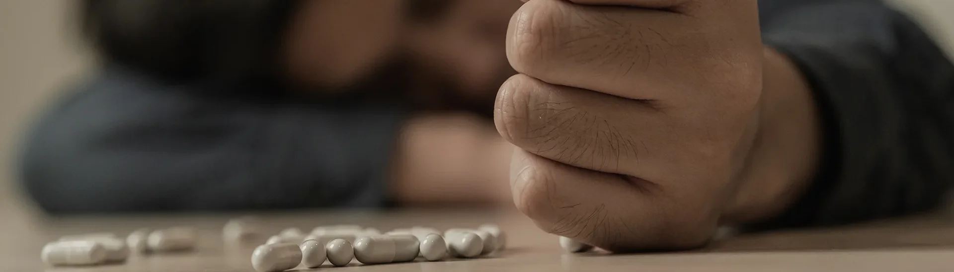A man struggling with opioid use with pills laying in front of him while his head is down on a desk.