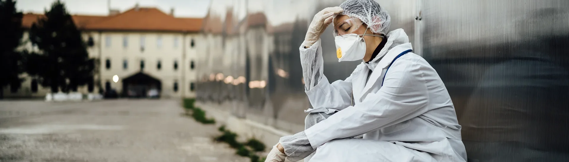 Stressed doctor sits outside with her hand on her head while wearing a mask.