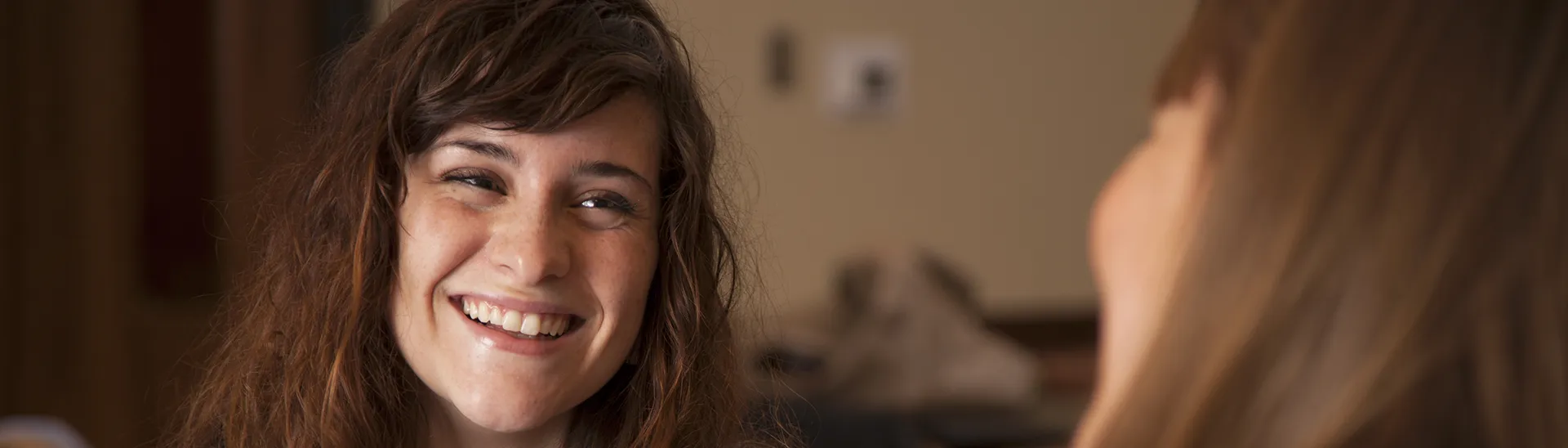A brunette girl smiles and laughs as she talks with her friend.