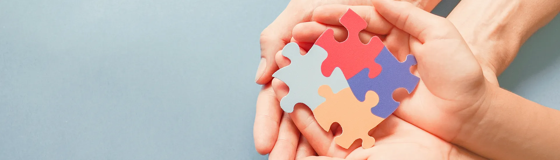 Two children's hands and two adult hands hold multi-colored puzzle pieces together.