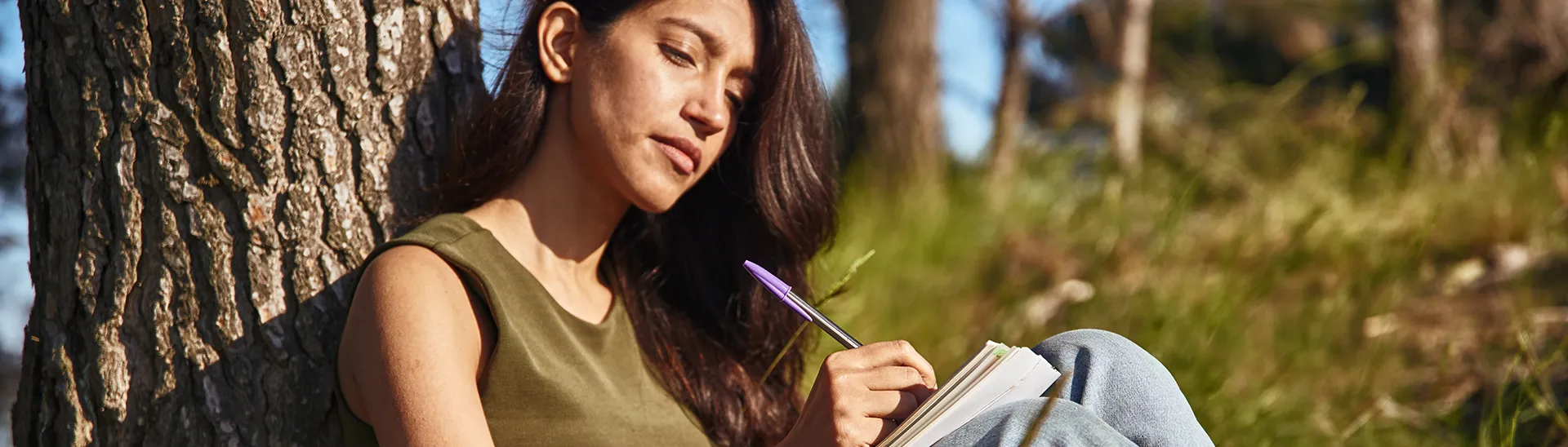 Woman sitting against a tree reading a book.