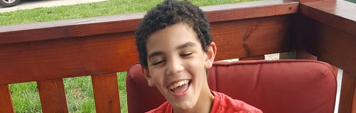 Un niño feliz sonriendo sentado en una silla al aire libre en una terraza.