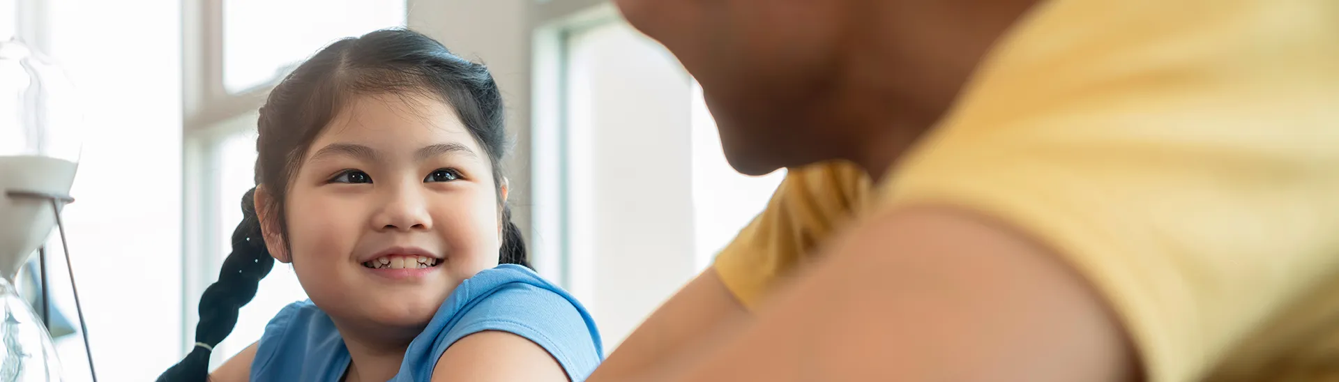 A young girl with pigtails, wearing a blue shirt talking to a man with a yellow shirt on.