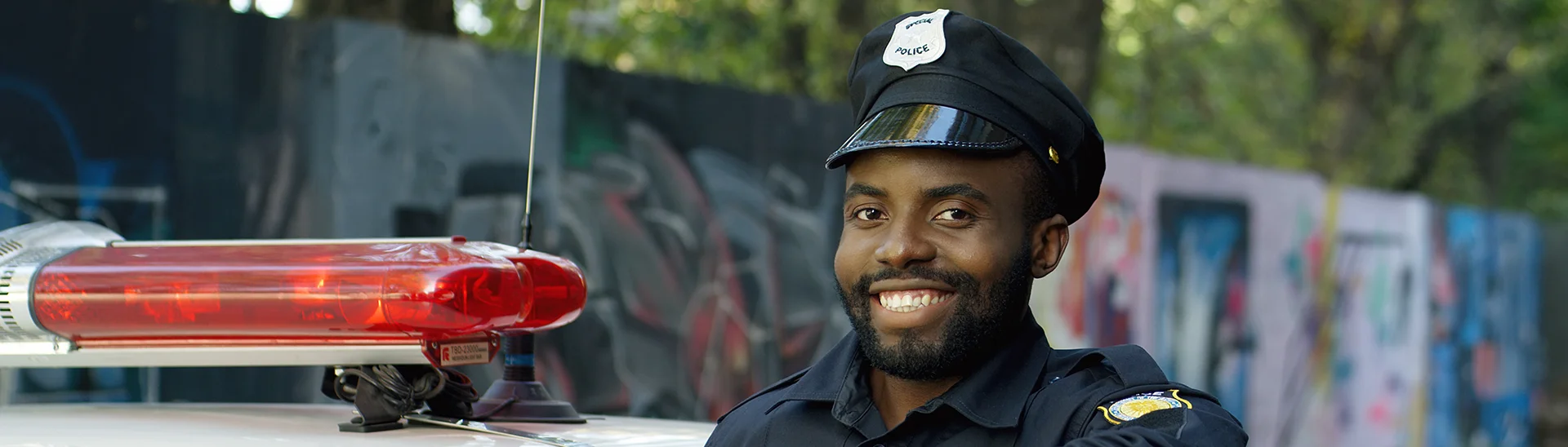 An African American police officer smiling while standing next to his patrol car.