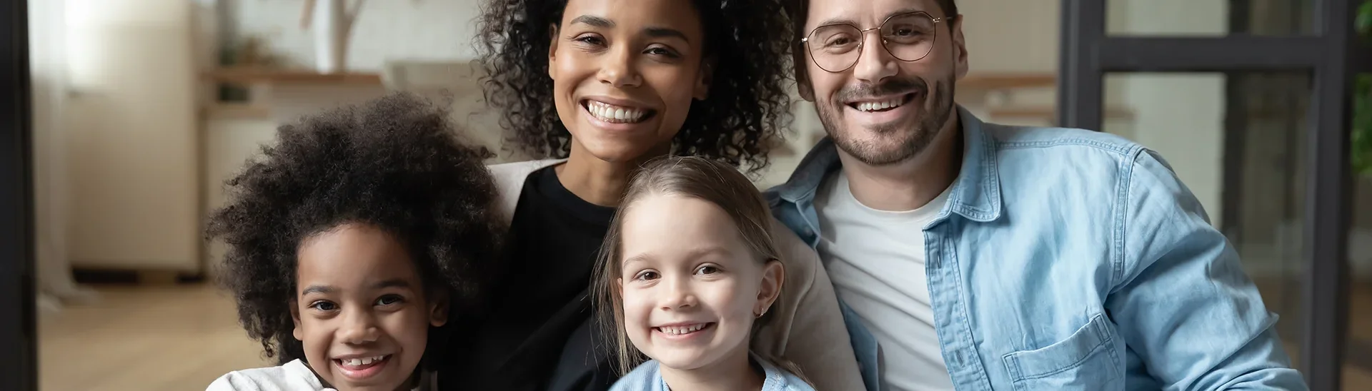 Familia multirracial de cuatro miembros sonriendo juntos en un sofá
