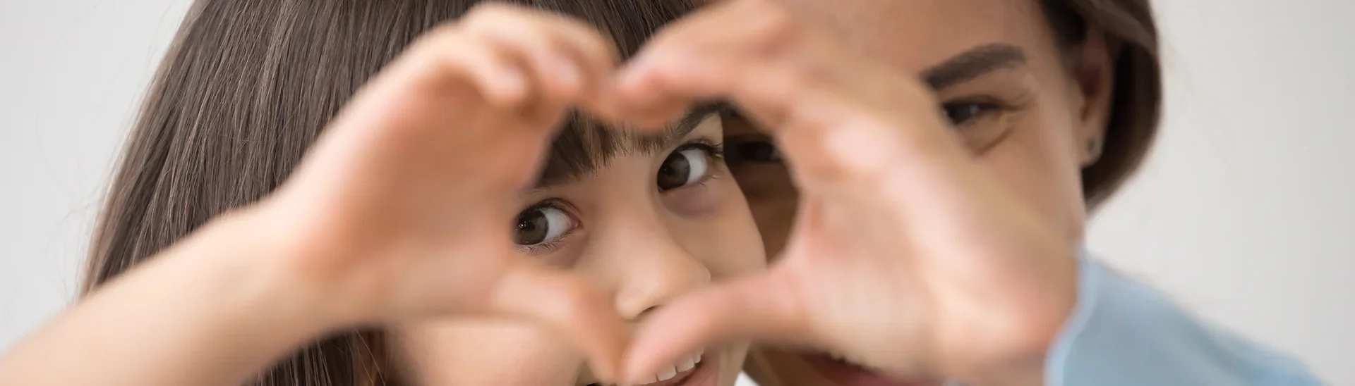 A mother and daughter holding their hands up in the shape of a heart together.