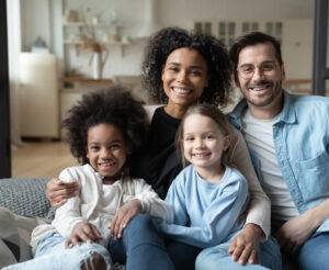 Multiracial family of four smiling together on a couch