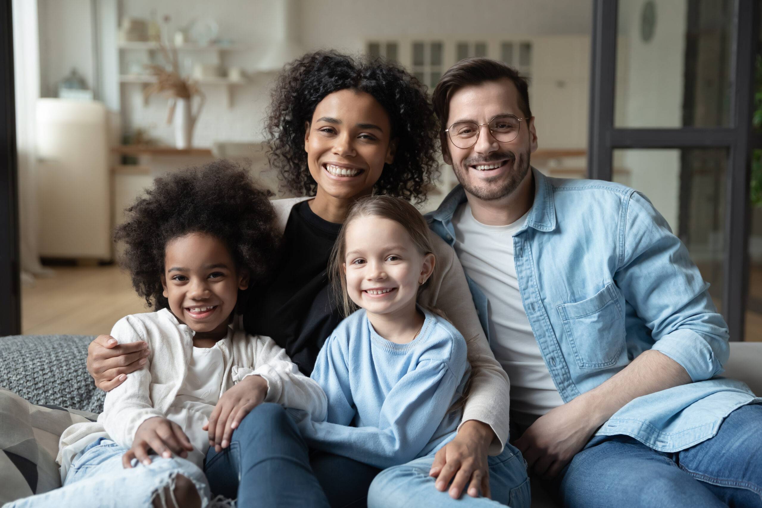 Multiracial family of four smiling together on a couch