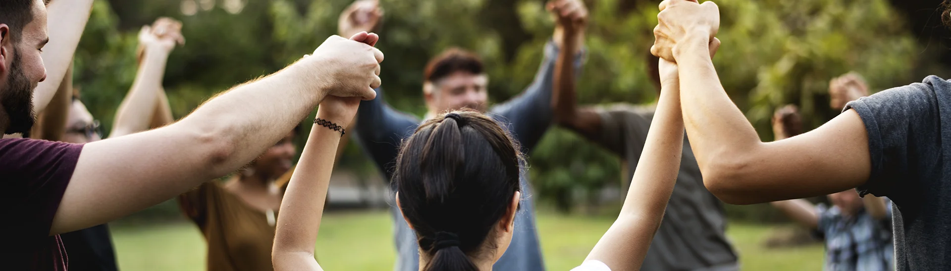 Grupo de personas de diferentes etnias en el exterior cogidas de la mano formando un círculo.