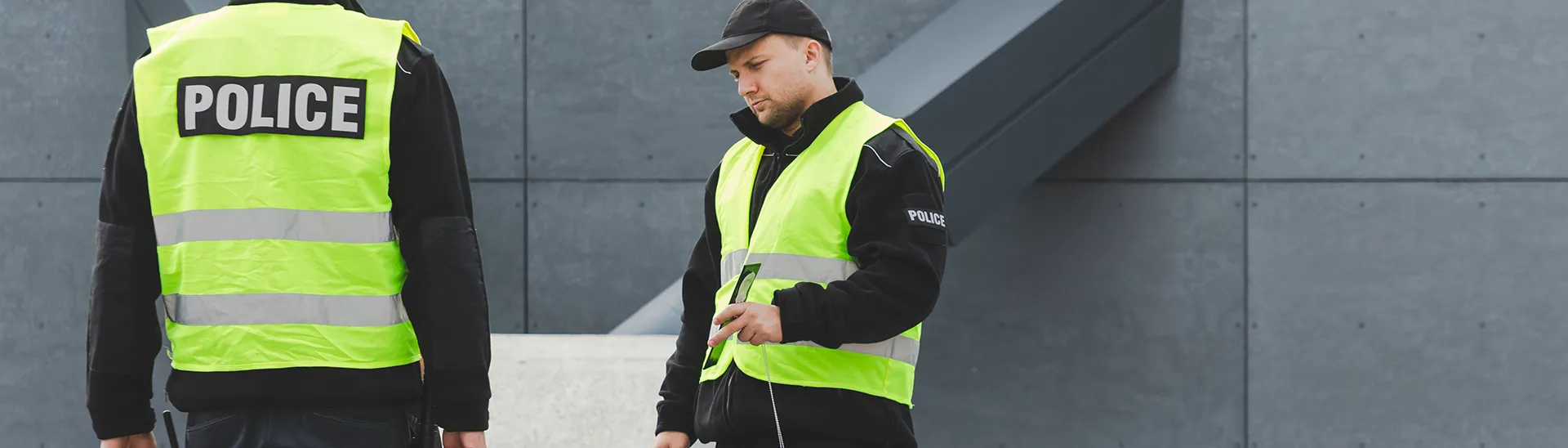 Two police officers in yellow vests calmly talking with a man sitting on a bench in a public outdoor area.