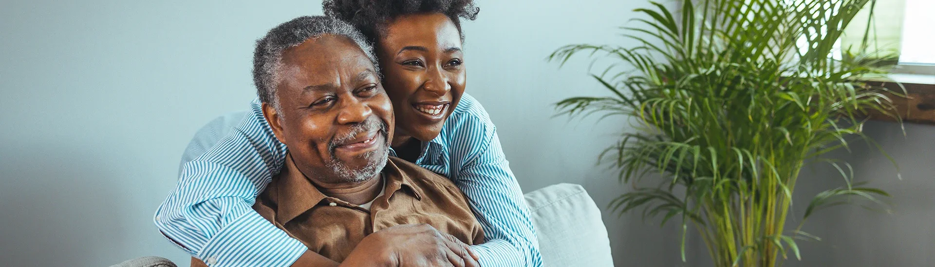 African-American woman smiling and hugging an older African-American man around his neck.