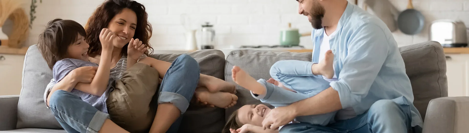 Happy family laughing on the couch. The dad is tickling the daughter and the mother is holding the son.