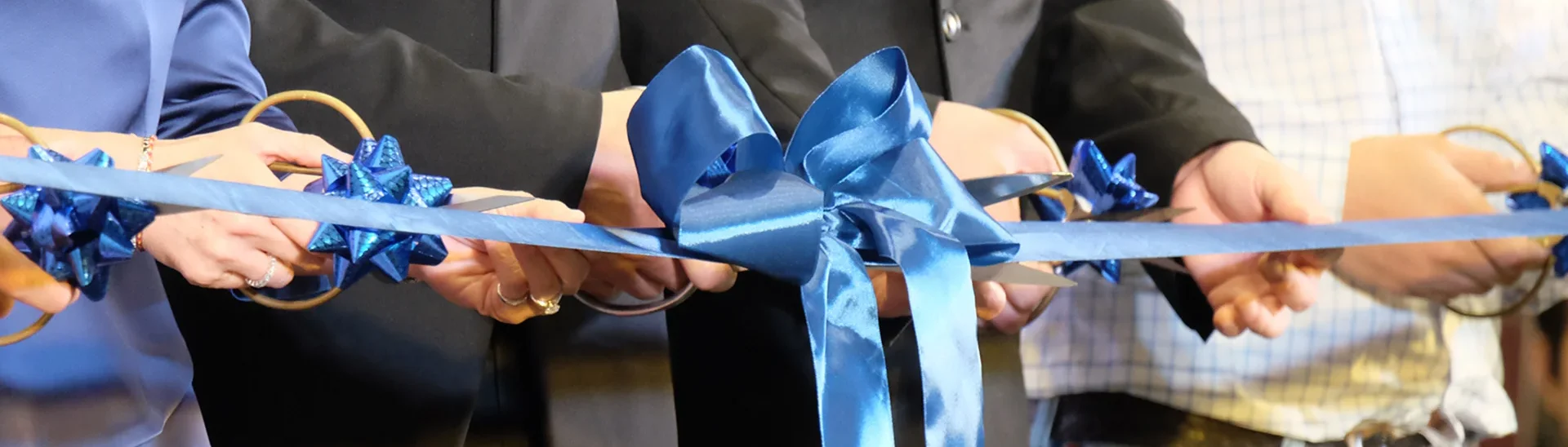 Grupo de personas cortando una cinta azul para inaugurar un nuevo local.