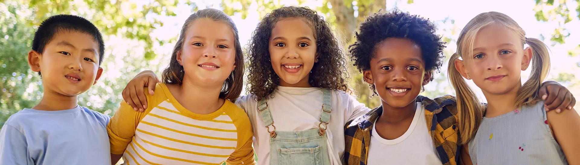 Group of children of different ethnicities smiling with their hands on each other's shoulder.