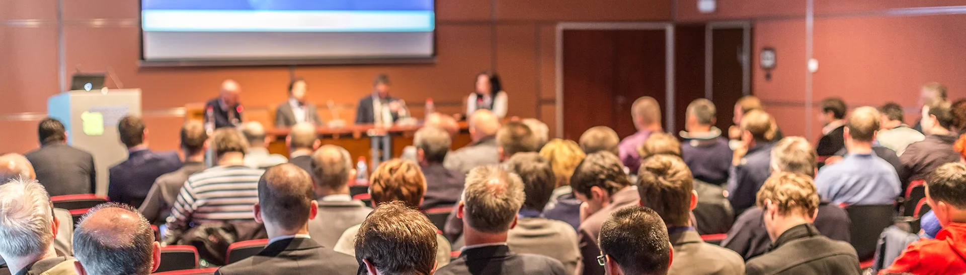View of a conference from behind the audience looking at the podium.