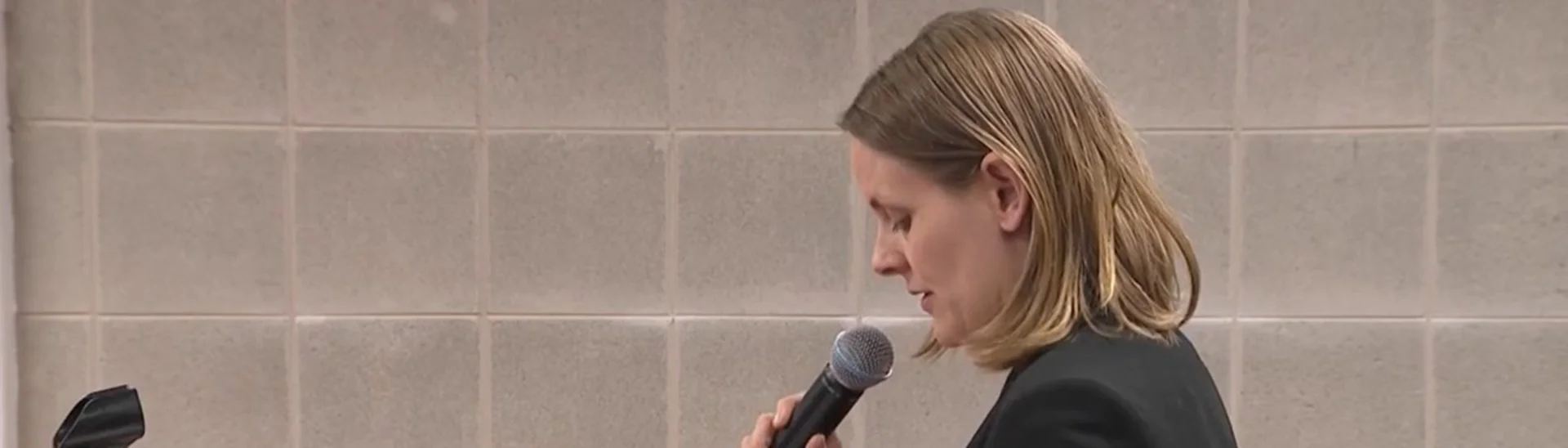 Press photo of Stephanie Craycroft-Andrews at a press conference holding a microphone.