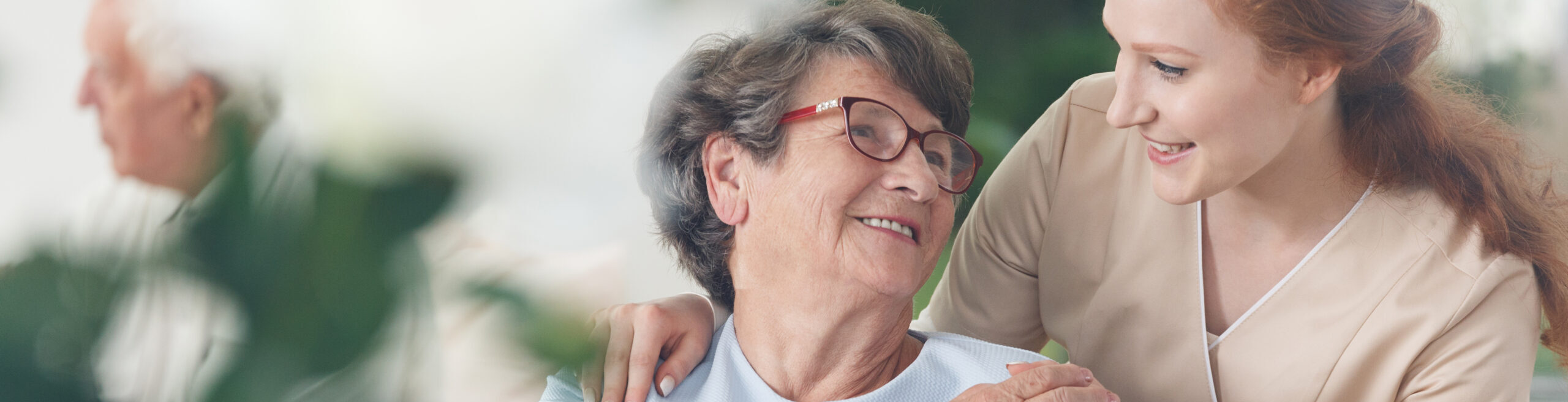 Professional helpful caregiver comforting smiling senior woman at Nursing Home