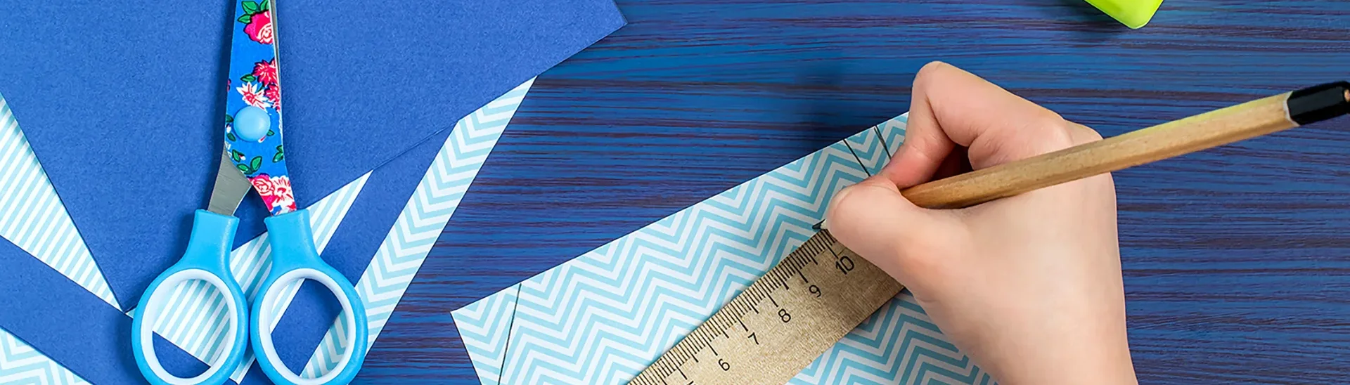 Someone creating art using a ruler, pencil, paper, cardboard paper, a pair of scissors, and glue.