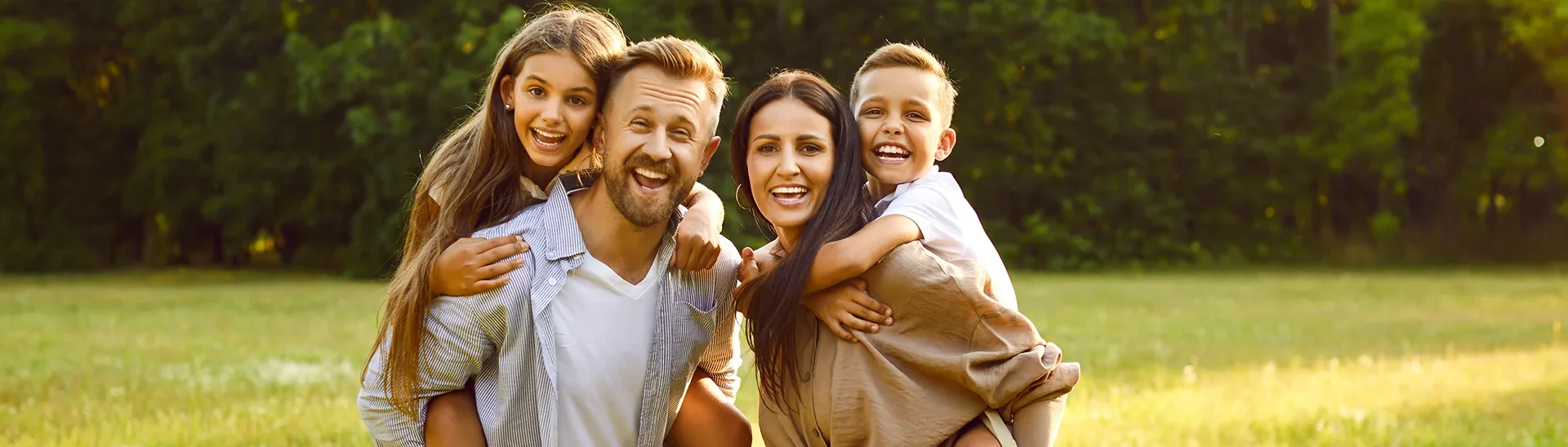 Mother and father happily smiling with their son and daughter smiling as well on their backs.