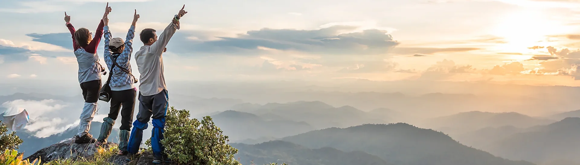 A group of people standing with their arms raised in happiness overlook at overlook of the mountains in the background.