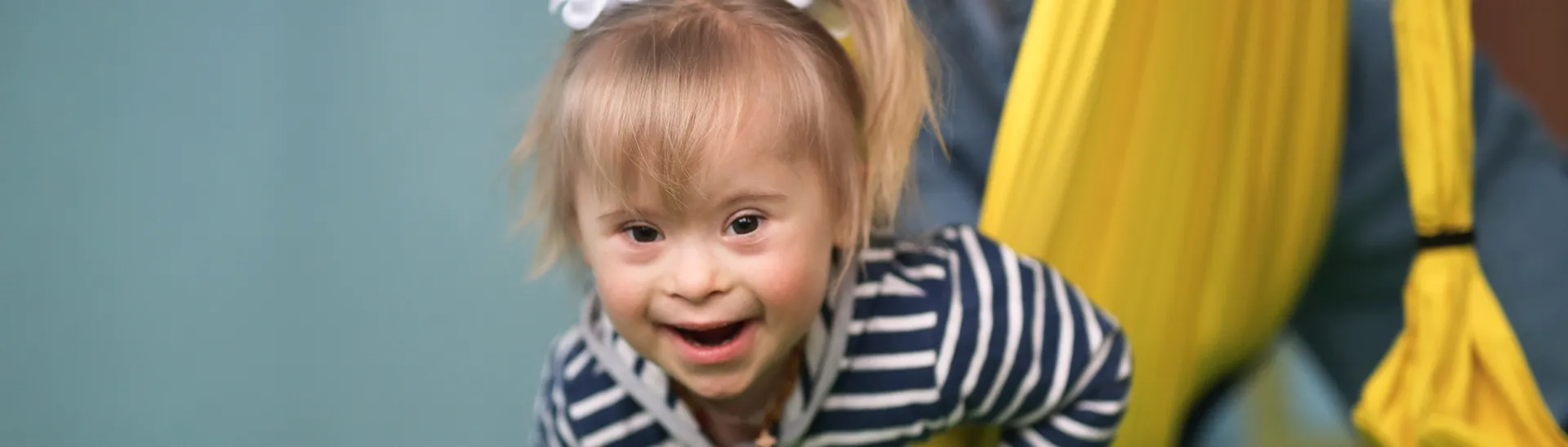 Young girl with down syndrome smiling happily, wearing a blue and white striped shirt.