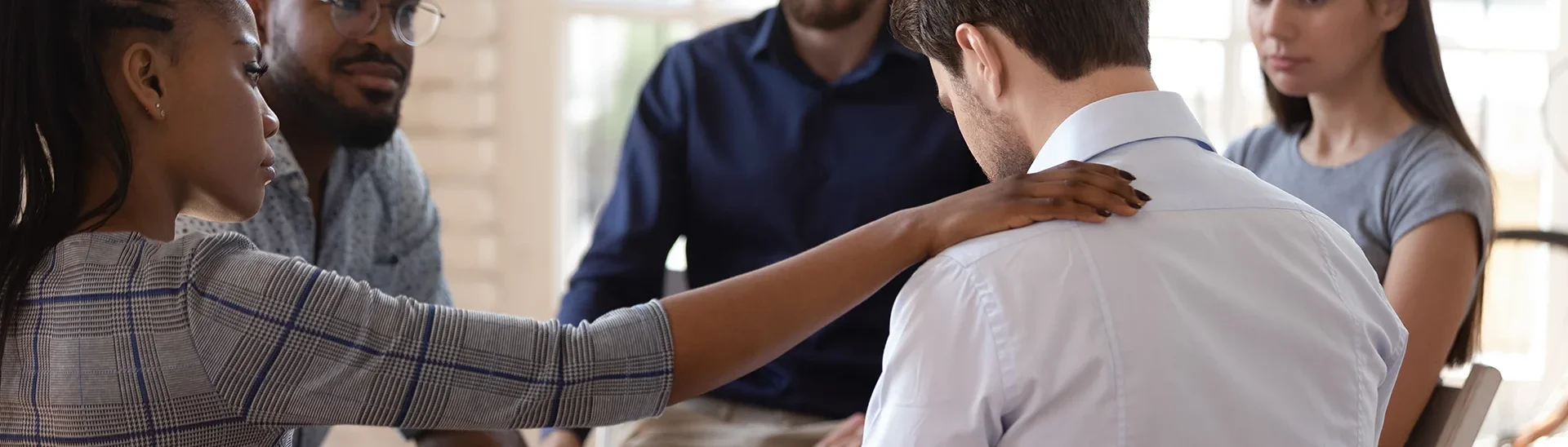 Support group of different men and woman of different backgrounds provided support to a man with his head bowed.