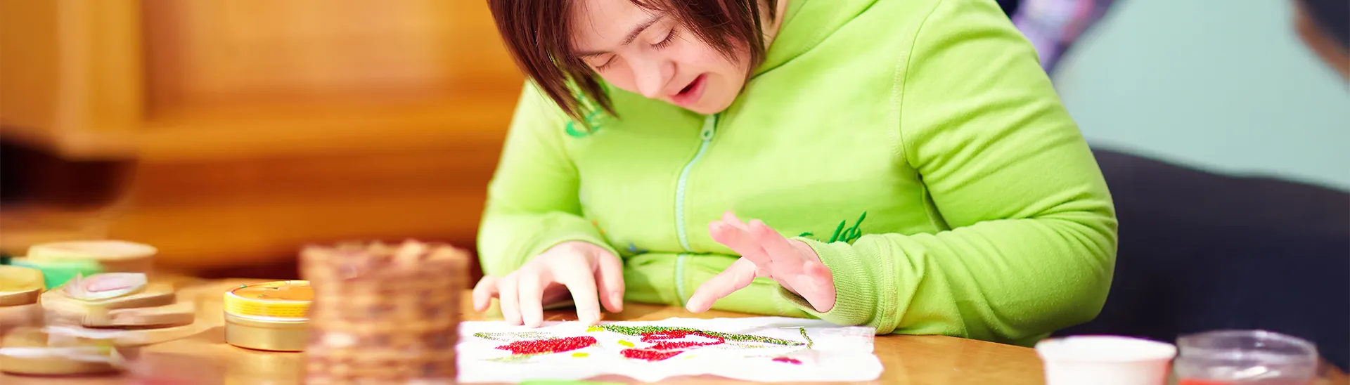A young female artist with down syndrome is working on a finger painting.