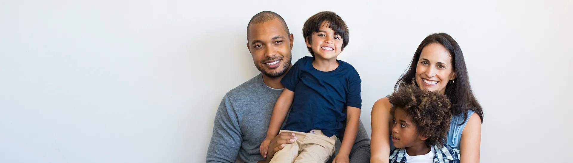 A diverse, young family sites together against a wall for a picture.
