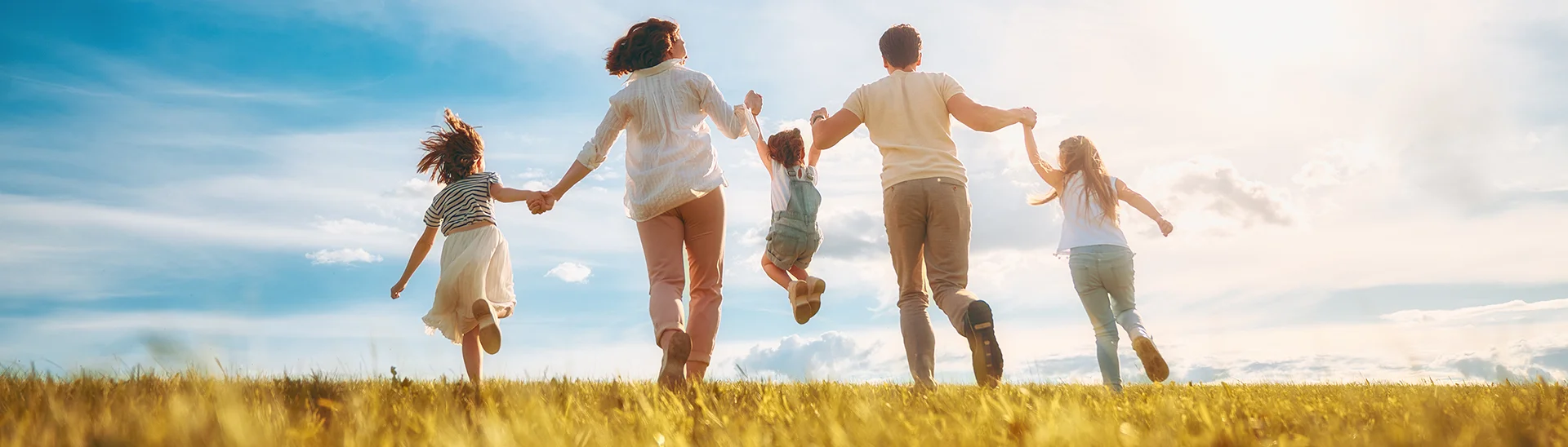 A large family of five are running hand-in-hand through a field with the youngest child swinging between mom and dad.