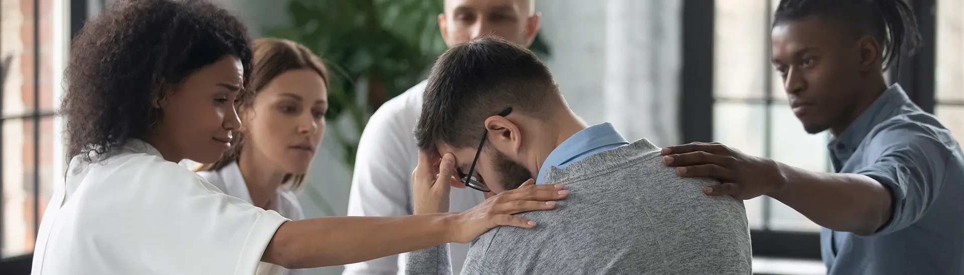 Un hombre recibe apoyo de un grupo en el que está con dos personas que le ponen las manos sobre los hombros.
