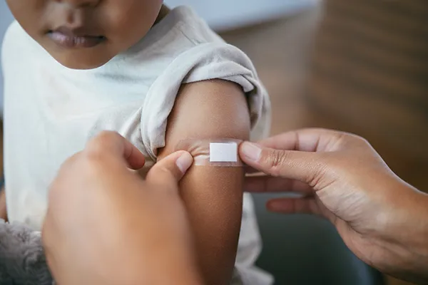 Child-Getting-Bandaid-Put-On_2293728981 Un niño al que le ponen una tirita en el brazo después de lo que puede haber sido recibir una inyección para una vacuna.