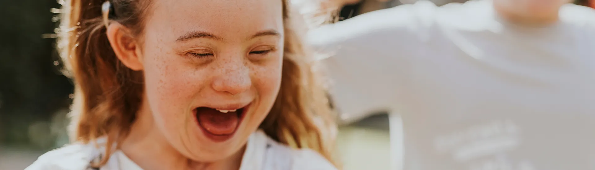 Una niña con síndrome de Down sonríe y ríe mientras crea burbujas con otro niño.