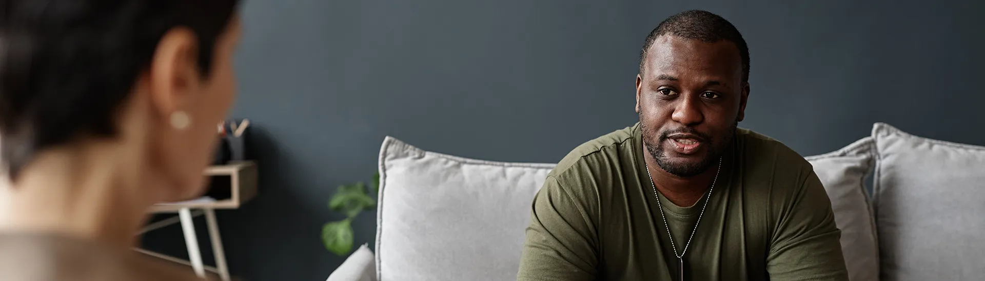 A man talking with a doctor or therapist about his problems while sitting on a grey couch.